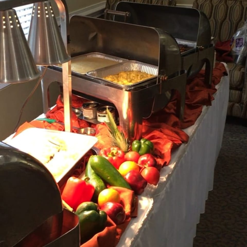 A soul food buffet with two chafing dishes, fresh vegetables, and red tablecloths.
