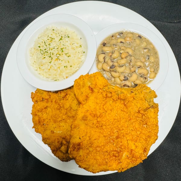Fried chicken cutlets with a side of white rice and black-eyed peas on a white plate.