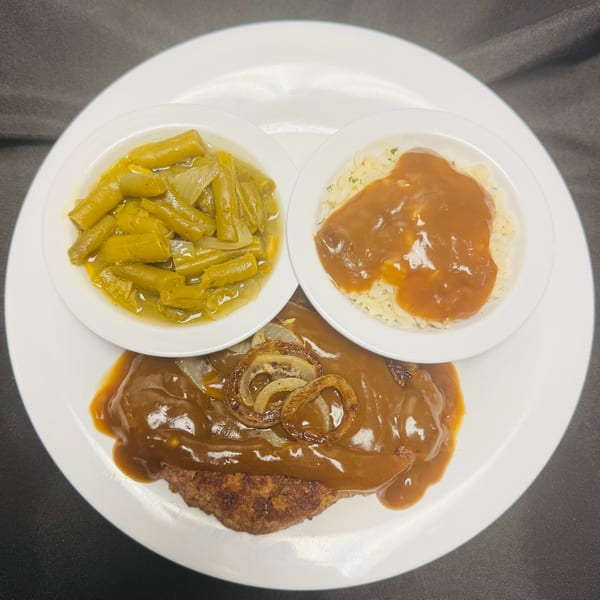 A Salisbury steak with gravy and onions, served with green beans and rice with gravy.