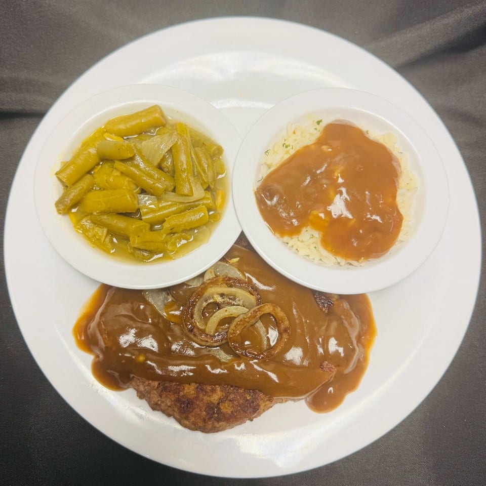 A Salisbury steak with gravy and onions, served with green beans and rice with gravy.