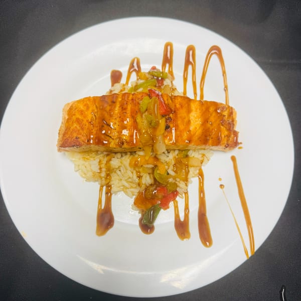 Glazed salmon fillet over rice with sautéed peppers and onions, drizzled with sauce.