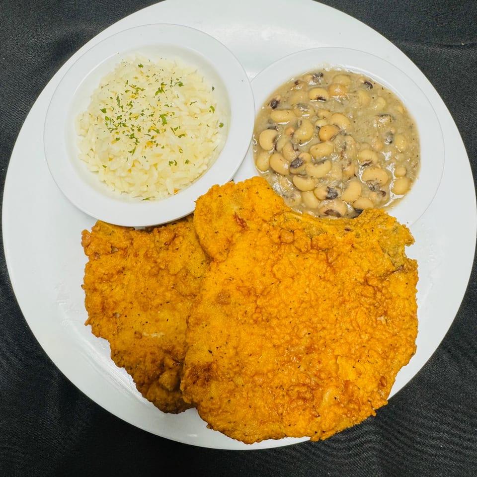 Two fried pork chops, a bowl of rice, and a bowl of black-eyed peas on a white plate.